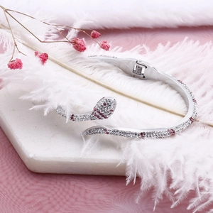 Bracelet serpent serti de cristaux sur marbre blanc avec plumes blanches et fleurs roses