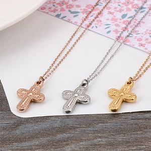 Three minimalist cross necklaces in rose gold, silver, and gold on a wooden background
