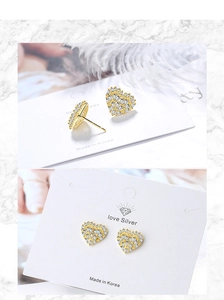 Macro detail of heart-shaped gold studs with sparkling cubic zirconia on marble background