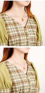 Detail of a minimalist gold heart-shaped pendant necklace worn on a V-neck plaid dress