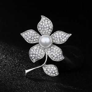 Macro detail of silver floral brooch with sparkling crystals and a white center pearl