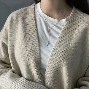 Detail of layered silver cross pendants necklace worn with beige knitted cardigan