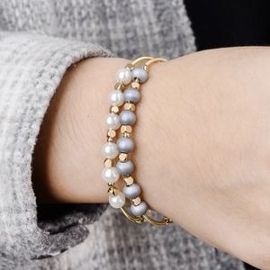 Gold stretch spring bracelet with white pearls and grey matte beads on wrist