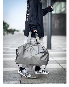 Man carrying a large grey waterproof nylon travel duffel bag in an urban street setting
