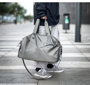Outdoor street lifestyle view of a grey nylon travel bag with crossbody strap and zipper
