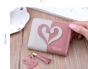 Detail of pink and grey bifold wallet with heart stitching and tassel on wooden table