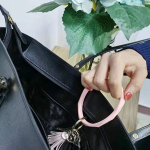 Pink silicone ring keychain with tassel attached to a black leather bag handle