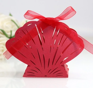 Red laser-cut shell shaped wedding favor box with silk ribbon on a white background