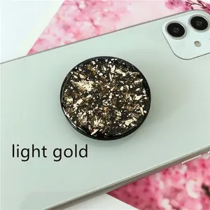Macro detail of round light gold foil glitter flake phone expansion stand on green smartphone