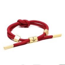 Detail of red braided couple bracelet with anchor engraved gold bead and steel tips