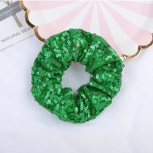 Glittery green sequin scrunchie hair tie on white background with decorative props