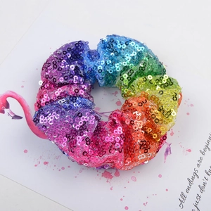 Close-up of rainbow sequin scrunchie hair tie on a decorative watercolor art background
