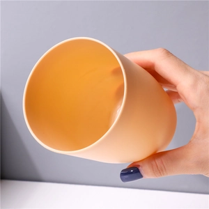 Minimalist orange plastic rinse cup held in hand against a sleek gray background