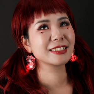 Close-up of red LED glowing star earrings with tassels on model in dark setting