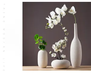 Nahaufnahme von drei mattweißen Keramikvasen mit Rillenstruktur und Blumendeko