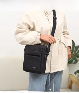 Men's black nylon crossbody bag with adjustable strap and front zipper pocket detail