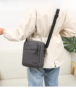 Male model wearing grey Oxford fabric crossbody bag with multi-pocket design in a home setting