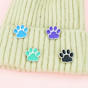 Set of four cute colorful paw enamel pins displayed on a beige knitted beanie hat