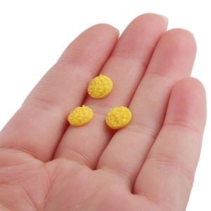 Macro shot of three 8mm yellow resin sparkling cabochons held in palm for scale