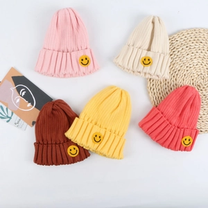 Flat lay of colorful macaron beanies with yellow smile patches on rib knit fabric