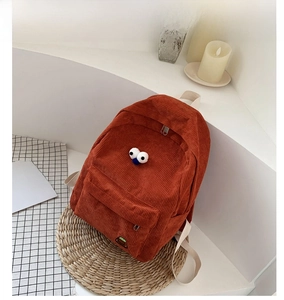 Detail of orange corduroy backpack featuring large 3D eye decor on a cozy prop background