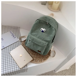 Green corduroy mini backpack with cartoon eye embroidery on a woven mat background