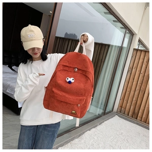 Detailed view of an orange corduroy backpack with cute cartoon eyes on the front pocket