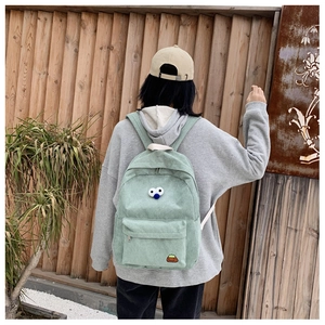 Detailed view of light green corduroy backpack featuring 3D eyes and cartoon embroidery