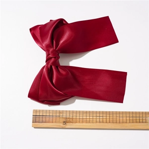 Detail view of a large red satin bow hair clip with measurement scale showing 14cm width