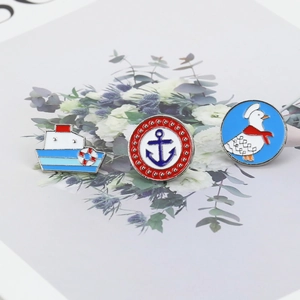 Detail shot of three nautical enamel pins including a boat, anchor, and cartoon goose