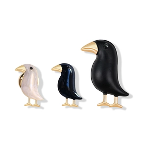 Three creative crow brooches in white, blue, and black enamel with gold details