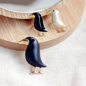 Three creative metal bird brooches in black and beige displayed on a wooden plate