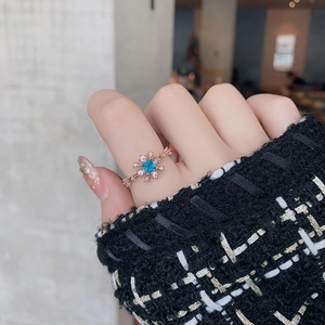 Macro detail of snowflake ring with blue gemstone on rose gold worn with tweed cuff
