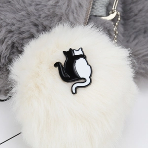 Macro detail of plush white faux fur charm featuring a black and white cat enamel badge
