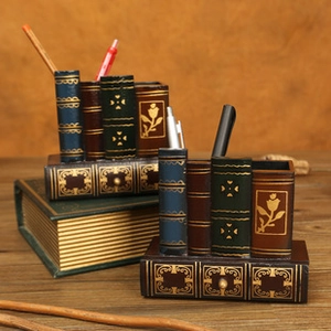 Close-up of vintage book-style resin pen holders with gold details on a wooden desk