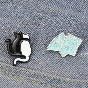 Blue origami enamel pin and black white cat pins set on blue denim fabric texture