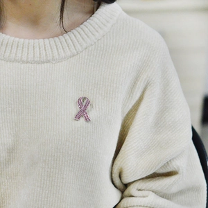 Pink ribbon brooch with sparkling rhinestones pinned on a beige corduroy sweater