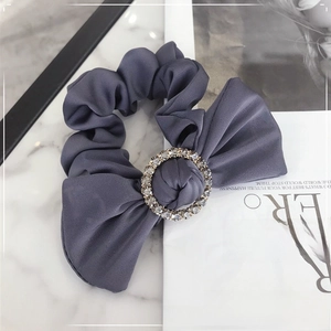 Close-up of grey satin scrunchie with sparkling rhinestone ring detail on marble surface