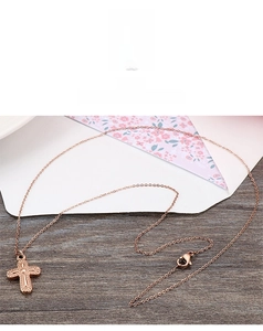 Detailed macro of rose gold 316L stainless steel cross necklace on a wooden background