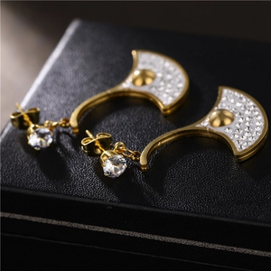 Gold ginkgo leaf drop earrings with white zircon inlays on black leather texture