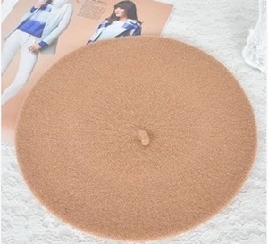 Detailed top view of a classic camel wool beret hat placed on decorative lace and a magazine