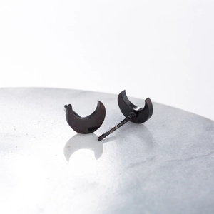 Detailed view of black matte crescent moon stud earrings on a grey stone base