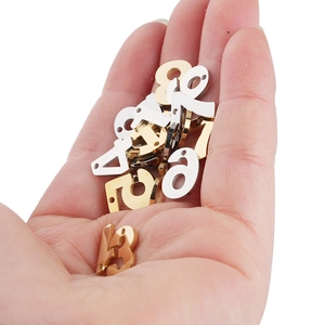 Hand holding assorted gold and silver stainless steel number charms on a white background