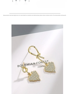 Detailed close-up of gold asymmetrical heart earrings with pavé crystals and knot design