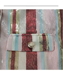 Dettaglio delle strisce di paillettes colorate e bottone a testa di leone dorato sulla giacca