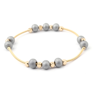 Detailed close-up of golden spring wire bracelet with matte grey beads on white background