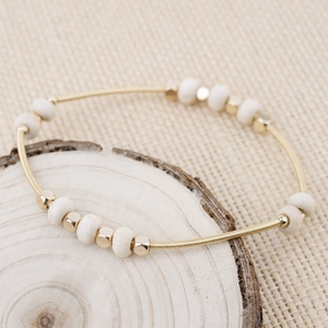 Golden spring wire bracelet with white ceramic beads on natural wood background