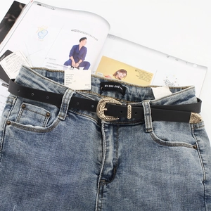 Vintage skinny black leather belt with ornate gold buckle on light blue denim jeans