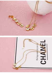 Macro shot of gold LOVE letter necklace and square zircon earrings on pink background