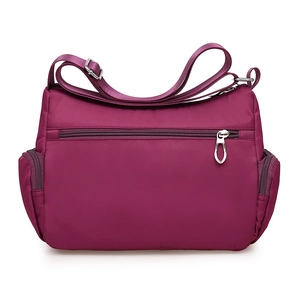 Purple nylon crossbody bag with quilted stitching and adjustable shoulder strap on white base